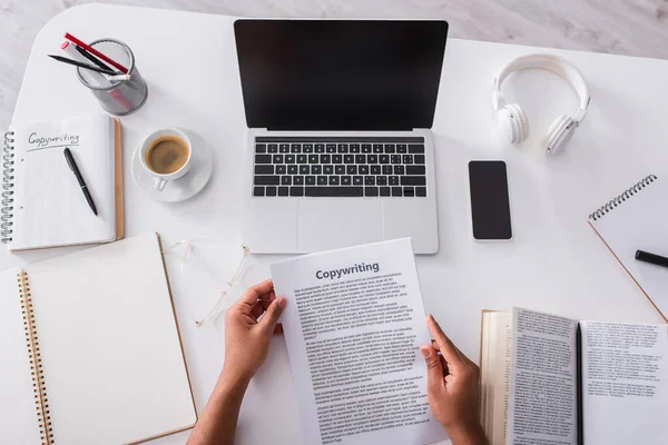 stock image Top view of man holding papers with copywriting lettering near notebooks and devices at home 