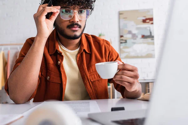 Indian Copywriter Eyeglasses Holding Cup Coffee Blurred Laptop Home — Foto Stock