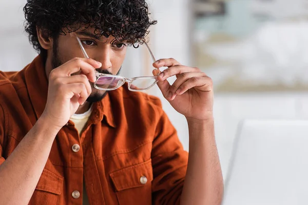 stock image Indian freelancer wearing eyeglasses near blurred laptop at home 