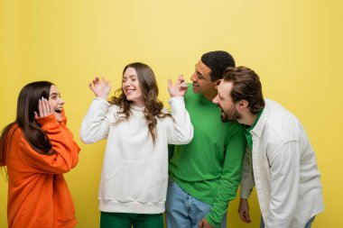 Smiling interracial people looking at friend on yellow background 