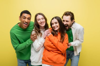 Positive multiethnic friends looking at camera on yellow background 