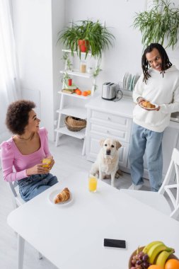 High angle view of smiling african american couple having breakfast near labrador at home 
