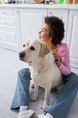 Young african american woman looking away near labrador at home 