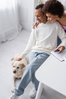 High angle view of smiling african american couple looking at labrador at home 