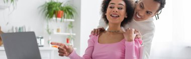 Cheerful african amercan freelancer pointing at laptop near boyfriend at home, banner 