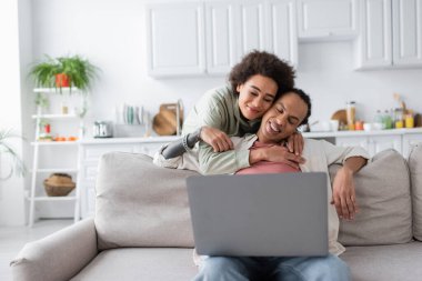 Young african american woman hugging boyfriend wit laptop at home 
