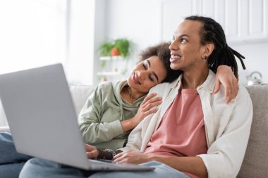 African american woman hugging boyfriend near laptop at home  clipart