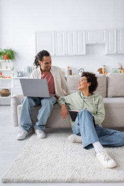 Cheerful african american couple with notebook and laptop talking at home 