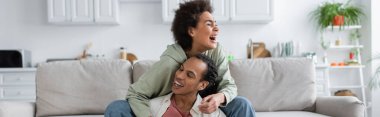 Excited african american woman hugging boyfriend while siting on couch at home, banner 