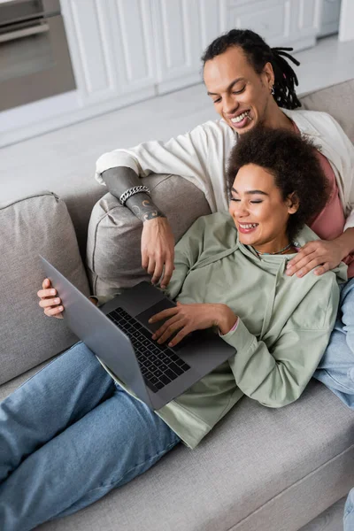 High angle view of excited african american couple using laptop on couch