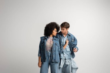 curly african american model touching denim jacket of young man isolated on grey 