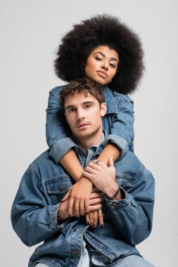 curly african american model looking at camera and hugging stylish man isolated on grey 