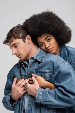 curly african american woman embracing stylish man in denim clothes isolated on grey 