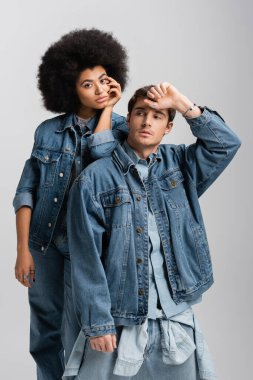 curly african american woman standing with man in denim outfit isolated on grey