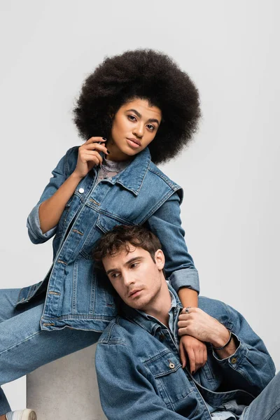 stock image curly african american woman sitting with man in denim outfit isolated on grey 