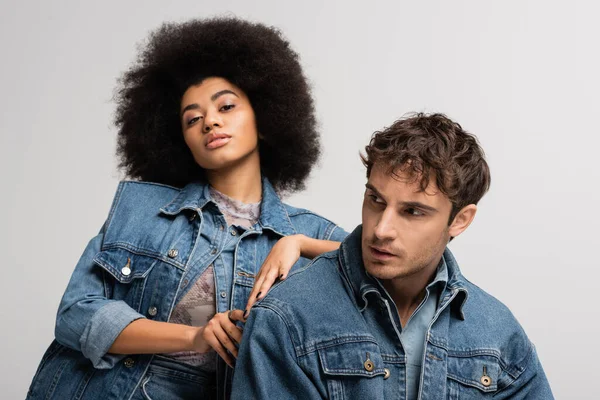 stock image brunette african american woman looking at camera and leaning on man in denim outfit isolated on grey 