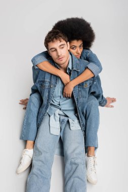 high angle view of stylish african american woman sitting and hugging stylish man in denim clothes on grey 