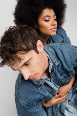 young man looking away near african american woman on blurred background isolated on grey 
