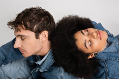 high angle view of african american woman with closed eyes leaning on back of man in denim clothes isolated on grey  clipart