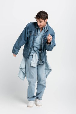 full length of stylish man in denim jacket and jeans posing on grey 