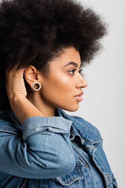 side view of curly african american woman in denim jacket looking away isolated on grey