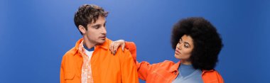 Stylish african american woman looking at man isolated on blue, banner 