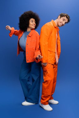 Full length of cheerful and stylish multiethnic models posing on blue background