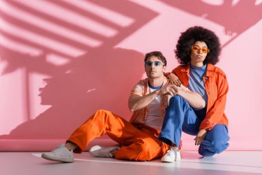 Fashionable multiethnic couple on pink background with shadow and light 