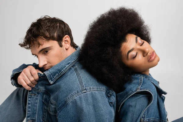 african american woman with closed eyes leaning on back of man in denim clothes isolated on grey
