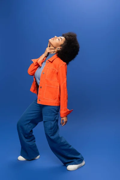 Fashionable African American Woman Jacket Pants Touching Neck Blue Background — Zdjęcie stockowe