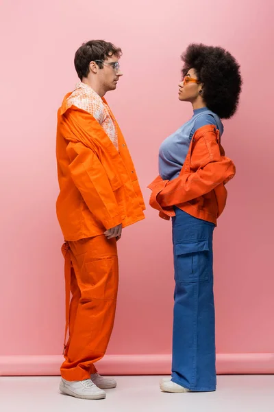 stock image Side view of trendy interracial couple in sunglasses looking at each other on pink background 