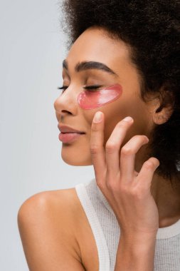 young african american model with closed eyes and collagen eye patches holding hand near face isolated on grey