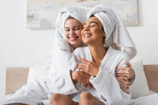 Joyful Interracial Women White Terry Bathrobes Towels Embracing Closed Eyes — Stock fotografie