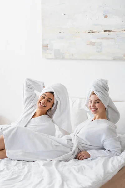 흰옷을 침대에서 쉬면서 카메라 앞에서 미소짓고 아름다운 인종간 여성들 — 스톡 사진