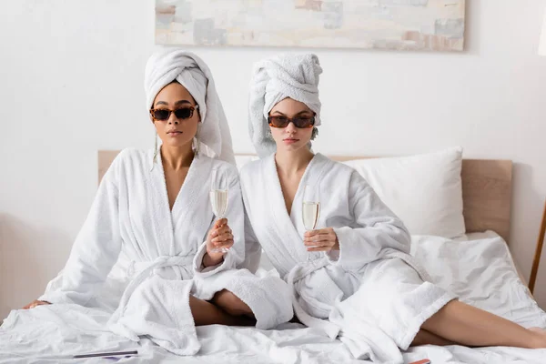 Young Multiethnic Women White Bathrobes Sunglasses Sitting Champagne Glasses Looking — 스톡 사진