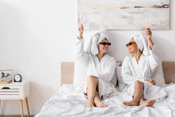 Full Length Joyful Multiethnic Women Terry Bathrobes Sunglasses Sitting Bed — 스톡 사진