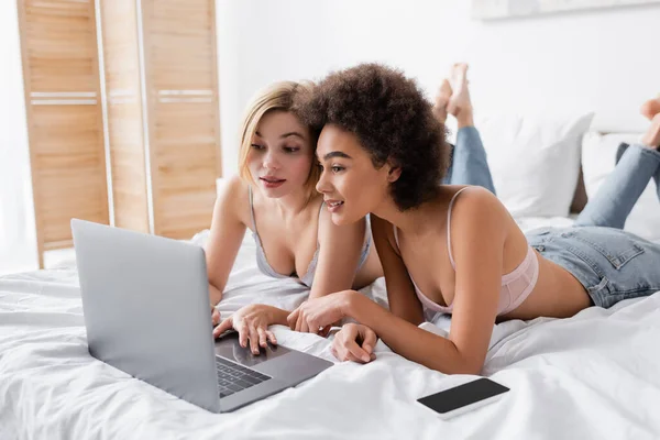 Young Interracial Women Lingerie Jeans Lying Bed Using Laptop Smartphone — 스톡 사진
