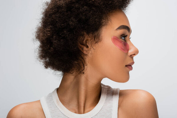 profile of brunette african american woman with hydrogel eye patch looking away isolated on grey