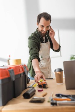 Akıllı telefondan konuşan pozitif marangoz atölyede cetvel alıyor. 