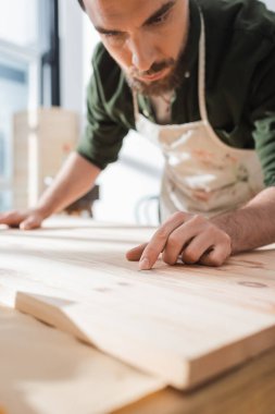 Carpenter in blurred apron touching surface of wooden board 