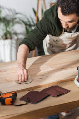 Bearded craftsman sanding wooden board near ruler in workshop  clipart