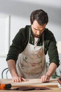 Brunette craftsman in apron sanding wooden bard  clipart