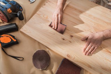 Top view of carpenter sanding wooden board near tools on table 