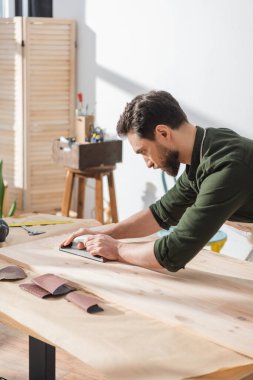 Side view of carpenter sanding surface of wooden board on table 