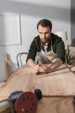 Restorer in dirty apron sanding wood in workshop  clipart