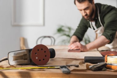 Tools on table near blurred restorer working with wood in workshop 