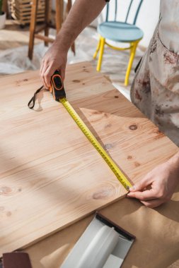 Önlüklü marangozun atölyedeki ahşap tahtaları ölçümlemesi. 