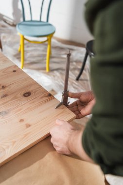 Cropped view of restorer measuring wooden board with calipers in workshop  clipart