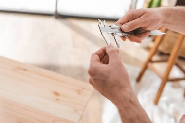 Cropped view of carpenter holding calipers near blurred wooden board in workshop 
