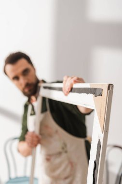 Blurred carpenter holding wooden picture frame in workshop 